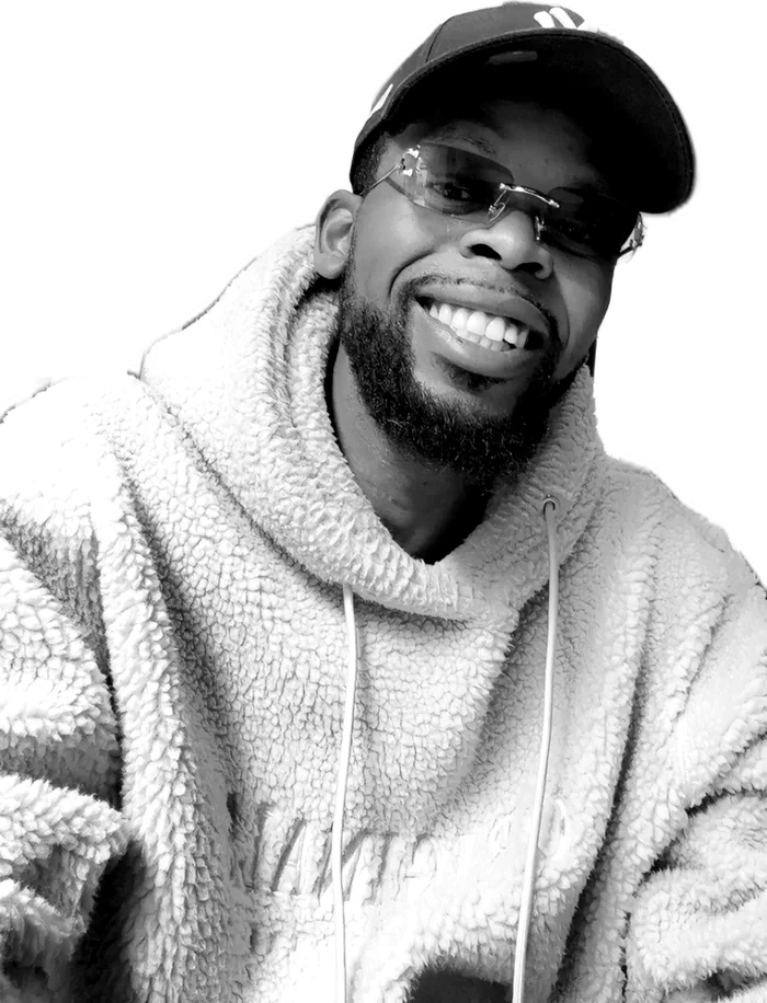 Portrait d'Anthony Ndekina Elibo en noir et blanc, souriant, casquette et lunettes.